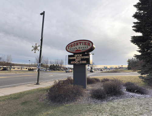Sign for Frontier Steak House indicating it's open on Thanksgiving from 10:43 AM to 3:00 PM, with a cloudy sky in the background.