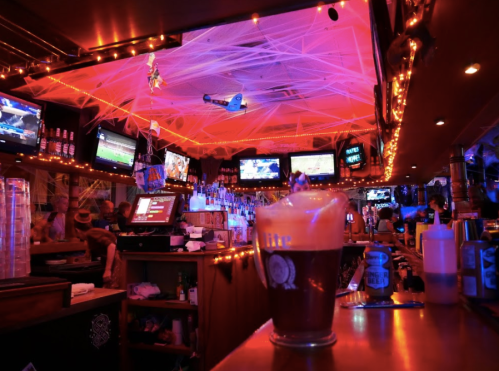 A vibrant bar scene with colorful lights, multiple screens, and a frothy beer in the foreground.