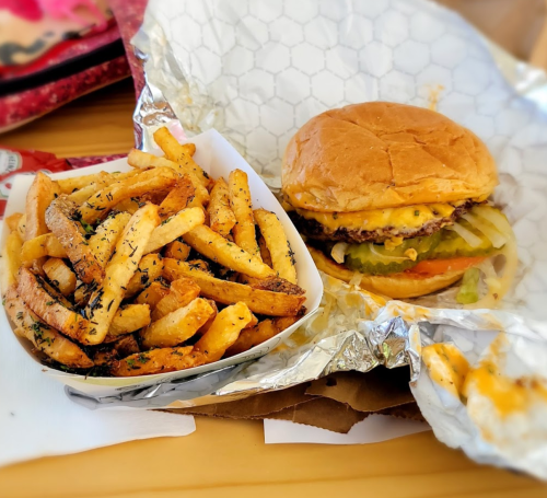 A delicious cheeseburger with pickles and a side of seasoned fries in a takeout container.