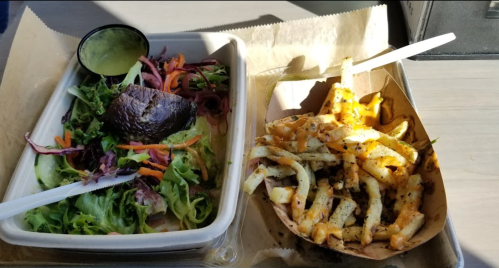 A salad with mixed greens and avocado alongside a tray of loaded fries topped with cheese and seasoning.