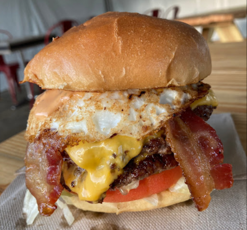 A delicious burger with a beef patty, melted cheese, bacon, tomato, and a fried egg on a toasted bun.