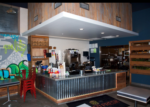 A modern restaurant interior featuring a metal counter, wooden accents, and colorful wall art.