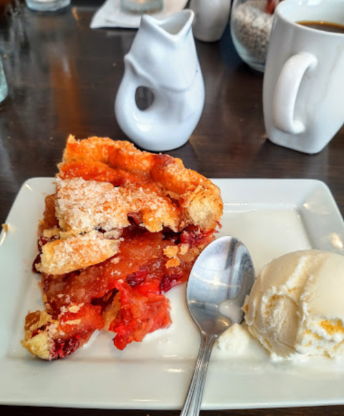 A slice of fruit pie with a flaky crust, served with a scoop of vanilla ice cream on a white plate.