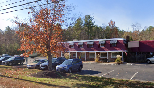 A red and white building with a tree and parked cars in front, set against a backdrop of autumn foliage.