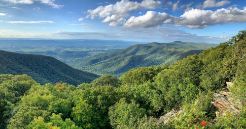 A panoramic view of lush green mountains and valleys under a blue sky with scattered clouds.