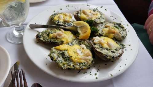 A plate of baked oysters topped with spinach and cheese, garnished with lemon wedges and parsley.