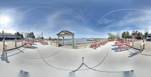 A panoramic view of a waterfront area with picnic tables, a gazebo, and a clear blue sky.