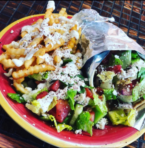 A plate with crinkle-cut fries, a foil-wrapped burrito, and a fresh salad drizzled with dressing and sprinkled with cheese.