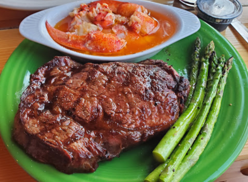 A plate featuring a juicy steak, asparagus, and a side of lobster in a buttery sauce.