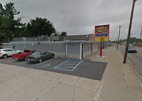 Exterior view of a sports bar with a sign, parking lot, and several cars parked outside on a cloudy day.