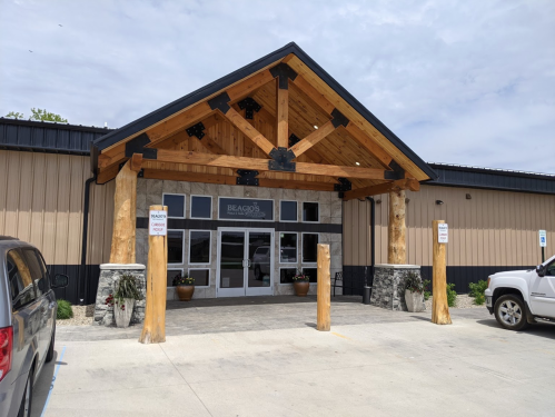 Exterior of a building with a wooden entrance, stone accents, and large glass doors, surrounded by planters.