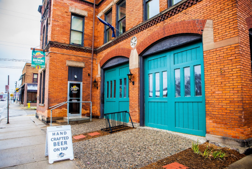 Exterior of a brick brewery with teal doors and a sign that reads "Hand Crafted Beer on Tap."