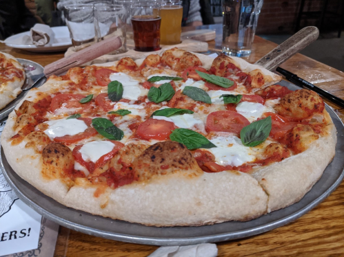 A freshly baked pizza topped with tomatoes, mozzarella, and basil on a metal tray, served in a rustic setting.