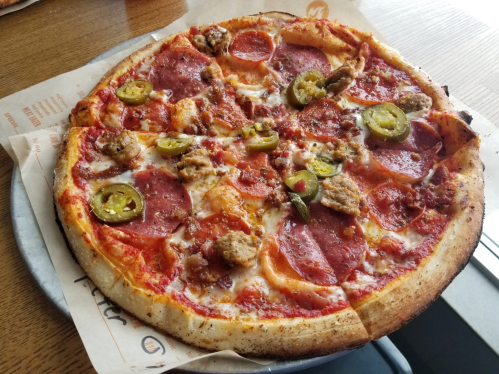 A freshly baked pizza topped with pepperoni, sausage, jalapeños, and melted cheese on a golden crust.