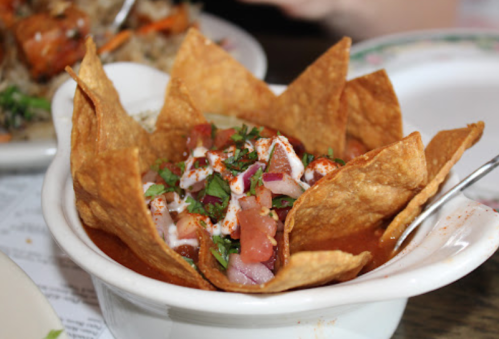 A bowl of tortilla chips filled with salsa, topped with diced tomatoes, onions, and a drizzle of cream.