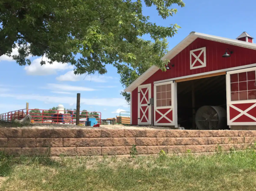 A red barn with white trim sits beside a grassy area, under a blue sky with scattered clouds.