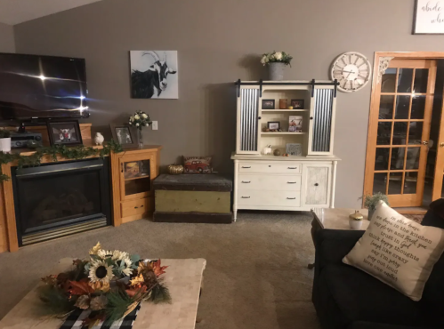 Cozy living room with a fireplace, decorative shelves, a coffee table with flowers, and a clock on the wall.