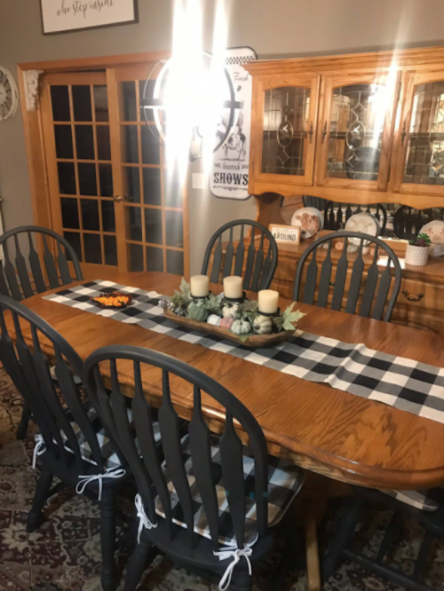 A dining room with a wooden table, black chairs, and a checkered table runner, decorated with candles and autumn accents.