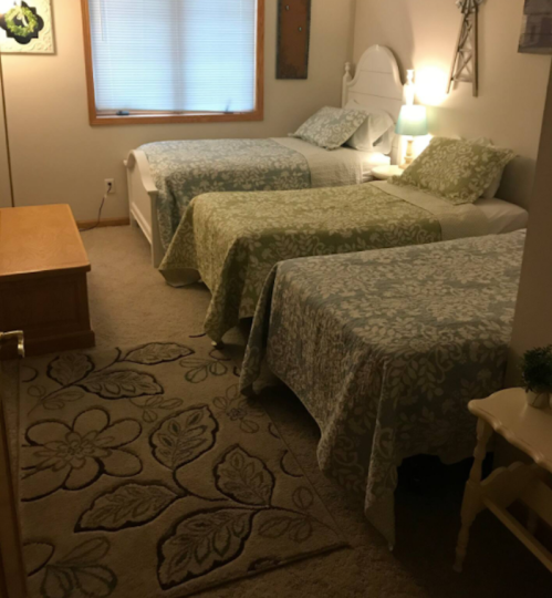 A cozy bedroom with three beds, each covered in floral-patterned quilts, and a soft rug on the carpeted floor.