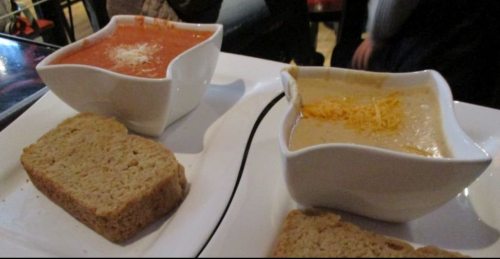 Two bowls of soup, one tomato and one creamy, served with slices of bread on a white plate.