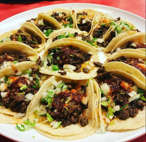A plate of tacos filled with seasoned meat, topped with onions, cilantro, and a spicy sauce.