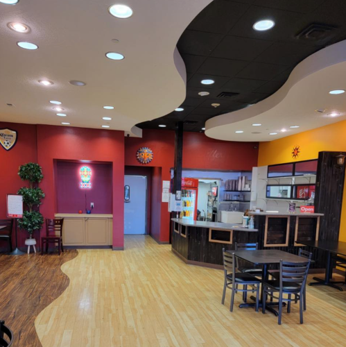 Interior of a colorful restaurant with curved ceiling, tables, and a counter. Bright lights and a welcoming atmosphere.