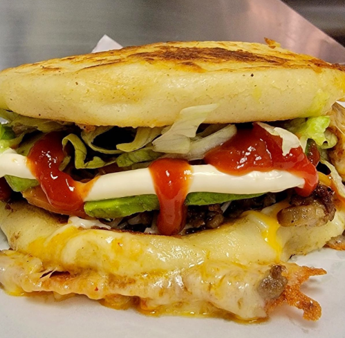 A close-up of a delicious arepa filled with meat, lettuce, sauces, and melted cheese, served warm.