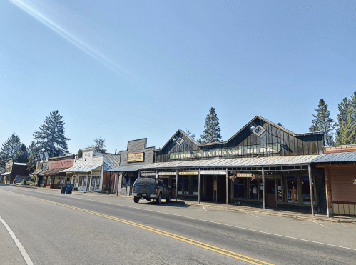 A quiet street lined with rustic storefronts and a black truck parked in front under a clear blue sky.