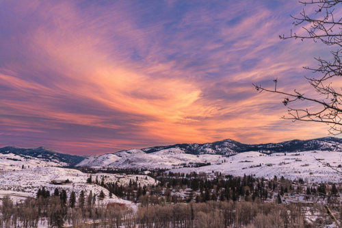 A vibrant sunset over snow-covered mountains and a valley, with colorful clouds illuminating the sky.