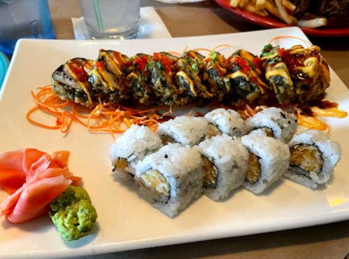 A plate of sushi featuring a colorful roll drizzled with sauce, accompanied by ginger, wasabi, and smaller sushi rolls.