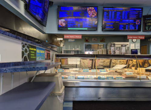 Interior of a food counter with digital menus, display cases, and a seating area. Brightly lit and inviting atmosphere.
