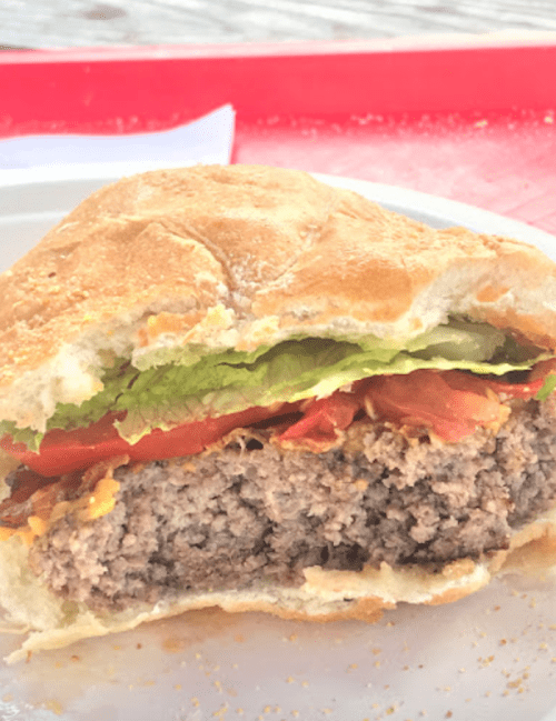 A close-up of a half-eaten burger with lettuce, tomato, bacon, and melted cheese on a toasted bun.