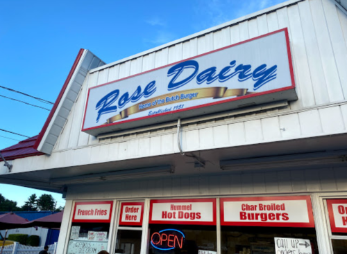 Sign for Rose Dairy, featuring "Home of the Bitch Burger," with a menu highlighting burgers, hot dogs, and fries.