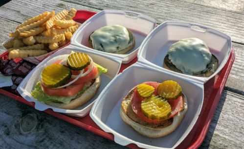 A tray with two cheeseburgers topped with lettuce, tomato, and pickles, alongside a serving of crinkle-cut fries.