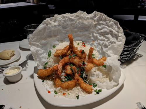 A plate of crispy shrimp on a bed of rice, topped with green onions and red peppers, served under a large crispy shell.