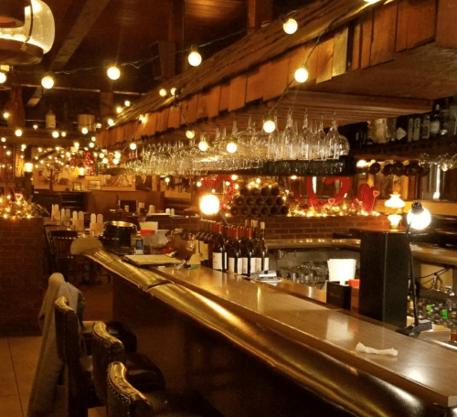 Cozy restaurant interior with warm lighting, a bar, hanging glasses, and a welcoming atmosphere.