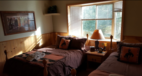 Cozy bedroom with two beds, wooden accents, a window with natural light, and rustic decor featuring horse motifs.