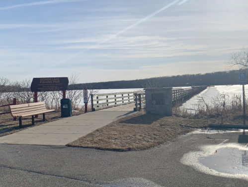 A view of Power Lake Fishing Pier with benches, a trash can, and a frozen lake under a clear sky.