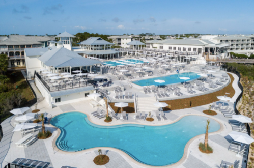 Aerial view of a resort with multiple pools, lounge chairs, and modern buildings under a clear blue sky.