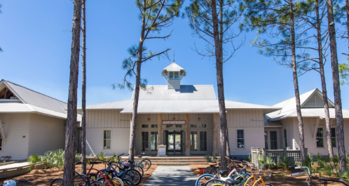 A modern building surrounded by tall pine trees, with bicycles parked in front and a clear blue sky above.