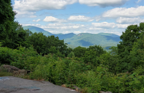 Lush green trees in the foreground with rolling blue mountains and a cloudy sky in the background.