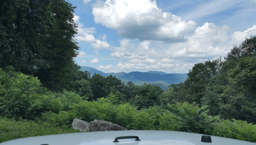 A scenic view of mountains and clouds, seen from a vehicle, surrounded by lush greenery.