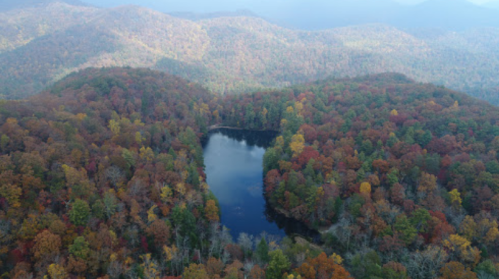 Aerial view of a serene lake surrounded by vibrant autumn foliage and rolling hills.