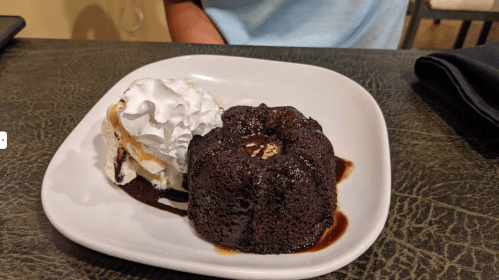 A chocolate lava cake with a scoop of vanilla ice cream and whipped cream on a white plate.