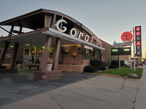 Exterior of Gorat's restaurant at dusk, featuring a retro sign and a welcoming entrance with greenery.