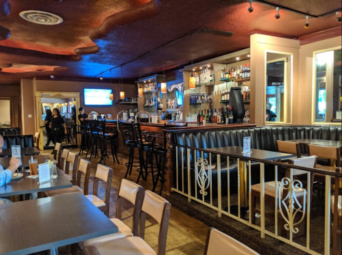 Interior of a restaurant with a bar, seating area, and a TV, featuring warm lighting and a cozy atmosphere.