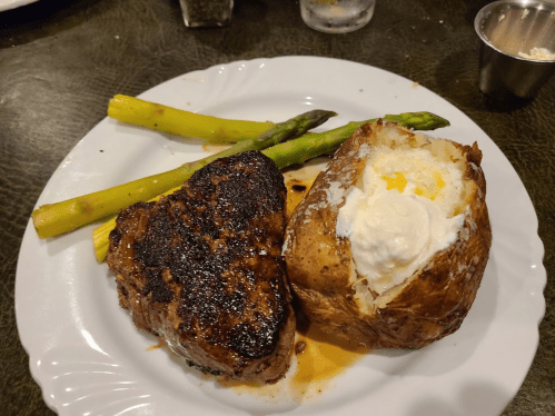 A plate with a grilled steak, baked potato topped with sour cream, and two asparagus spears.