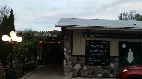 Exterior of Blackhawk Steak Pit restaurant, featuring stone walls, a sign, and decorative lights.