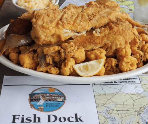A large plate of fried fish and hushpuppies, garnished with lemon, on a table with a map and a restaurant sign.