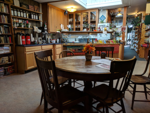 Cozy café interior with a wooden table, chairs, and shelves filled with books and various items. Warm, inviting atmosphere.